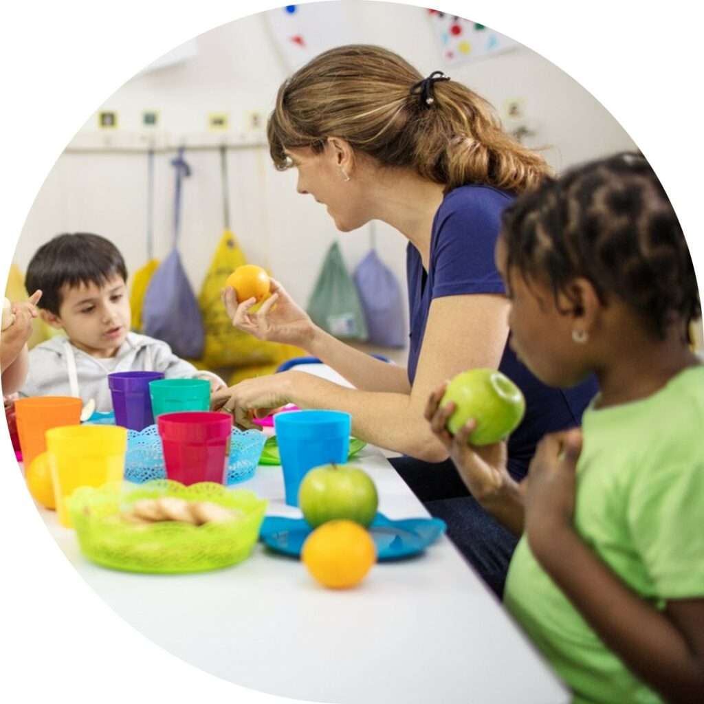 Erzieherin sitzt mit den Kindern in Kindergarten und hilft bei der Essensverteilung.